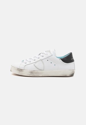 Witte leren sneaker met een zwarte hielaccent, geperforeerde details, ronde neus en een versleten, textuur van de zool, voorzien van een blauwe binnenvoering.