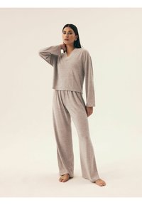 Szary zestaw dresowy z dzianiny składający się z długiego rękawa bluzki z dekoltem w kształcie V oraz szerokich spodni, o miękkiej teksturze i luźnym kroju.