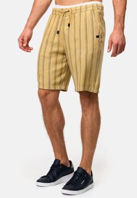 Shorts rayés beiges avec taille à cordon de serrage, présentant des rayures verticales noires et des poches latérales. Associés à des baskets bleu marine.