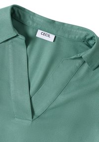 Grüner V-Ausschnitt mit genähtem Revers und weißem "CECIL" Markenlabel, das im Kragen eingenäht ist.