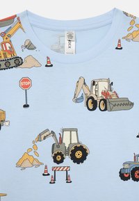 Chemise bleu clair avec des véhicules de construction dessinés, des cônes de signalisation, un panneau stop et des tas de terre dispersés sur le tissu.