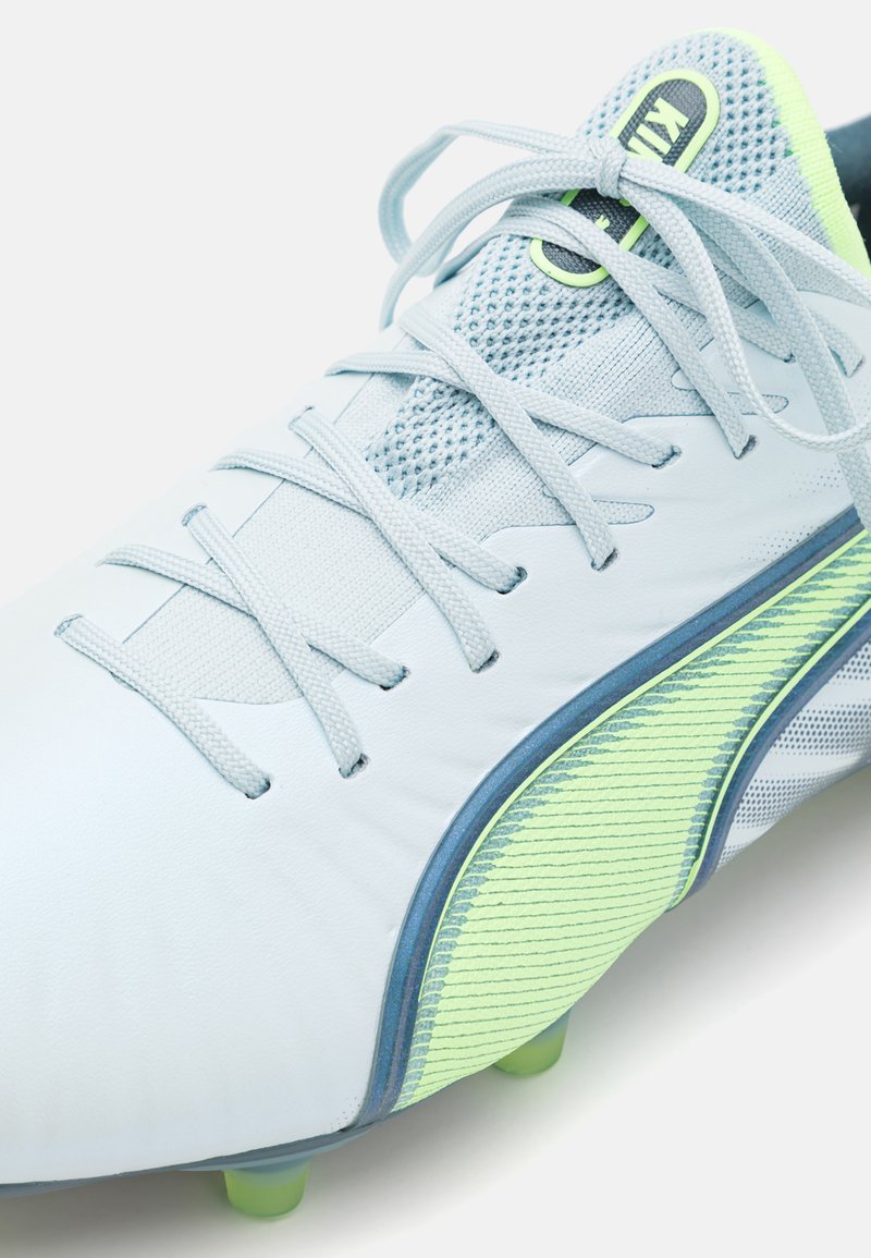 Scarpa da calcio azzurra chiara con tomaia testurizzata, inserti in rete e striscia verde. Presenta suola grigia e lacci per una vestibilità e supporto ottimali.