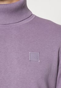 Närbild av en lavendelfärgad ribbad polotröja med en liten fyrkantig lapp märkt "BOSS" på bröstet.