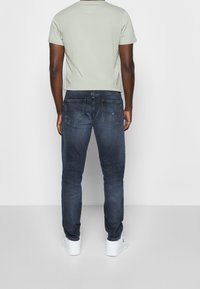 Mans ljusgröna t-shirt och mörkjeans med slim fit, som har två bakfickor och en enkel design. Bärs med vita sneakers.