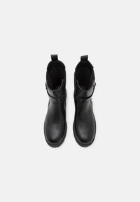 Bottes noires jusqu'à la cheville en cuir lisse avec une finition mate, présentant un détail de sangle sur le côté et des languettes pour un enfilage facile.