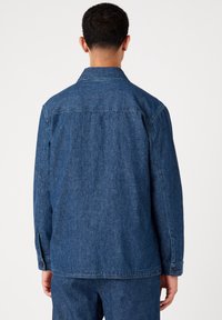 Tummansinisestä farkkutakista, jossa on klassinen kaulus, pitkät hihat ja napilliset hihansuut. Sisältää yksinkertaisen, tekstuuripintaisen kankaan sekä takakappaleen.