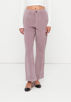 Femme portant un pantalon en velours côtelé mauve taille haute à jambes larges, associé à des ballerines slingback bicolores beige et noir.