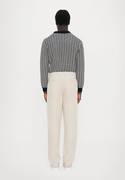 Long-sleeve striped black and white shirt with a black collar, paired with loose-fitting beige pants. Smooth texture, minimal detailing.