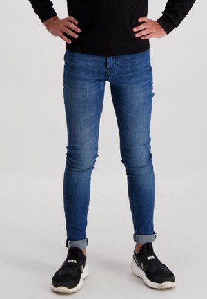 Blauwe denim skinny jeans met een vervaagde was, opgerolde boorden en een klassieke vijf-pocket ontwerp, gecombineerd met zwarte sportschoenen.