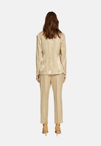 Costume en satin beige comprenant une veste ajustée et un pantalon droit, présentant une texture lisse et un design simple et élégant.