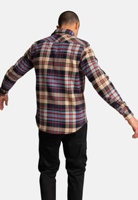 Koszula w kratę w odcieniach beżu, granatu i czerwieni, z kołnierzykiem zapinanym na guziki i długimi rękawami; materiał ma teksturowany wzór z kontrastującymi kwadratami.