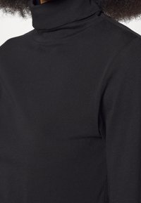 Schwarzer Rollkragenpullover aus weichem, elastischem Stoff. Merkmale sind eine figurbetonte Silhouette und lange Ärmel mit minimalen Nähten für ein glattes Erscheinungsbild.