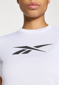 Tricou alb, ajustat, cu mâneci scurte, având un logo negru proeminent pe piept. Textură netedă și decolteu în formă de cerc.