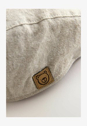 Beige Stoffkissen mit strukturierter Oberfläche und einem braunen Lederpatch mit einem Bärmotiv. Dezente Steppnähte verfeinern das Design.