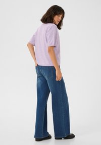 Top en tricot lilas à manches courtes avec une coupe décontractée, associé à un jean en denim bleu à jambes larges. Le jean dispose de poches arrière et d'une taille classique.
