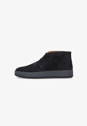 Stivaletti in suede neri con suole in gomma grigia, caratterizzati da punta rotonda, due asole per lacci e un accento cucito lungo il lato.