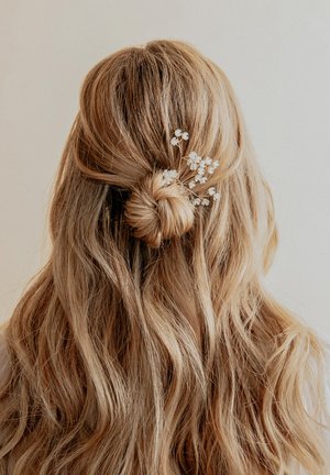 Capelli biondi lunghi e ondulati acconciati in un basso chignon, decorati con delicate fiori bianchi. Lo sfondo è neutro e non invadente.