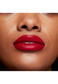 Rouge à lèvres mat éclatant sur des lèvres pleines, mettant en valeur une texture lisse avec une forme précise et des contours définis, illuminé sur un teint de peau chaud.