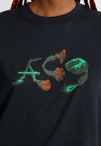 Juodas marškinėliai su stilizuotais "ACG" rašmenimis, pagamintais iš žalių ir oranžinių kaktusų iliustracijų ant priekio.