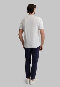 Maglietta bianca a maniche corte con collare a girocollo rigato, abbinata a pantaloni cargo blu navy e sneakers bianche. Il tessuto sembra leggero e morbido.