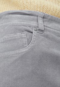 Pantalones de pana gris con un bolsillo visible, botón y detalles en la cintura. La tela tiene una superficie texturada y acanalada.