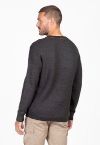 Dunkelgrauer strukturierter Pullover mit Rundhalsausschnitt und langen Ärmeln, ausgestattet mit einem gerippten Saum und Bündchen. Getragen über beigen Hosen.