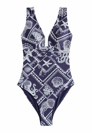 Žena v tmavomodrom plavkách s bielymi vzormi morských tvorov a mušlí stojaca pri vode pod jasnou oblohou.