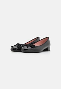 Ballerines en cuir verni noir avec un bout arrondi, ornées d'un nœud en corde noir décoratif sur le devant et d'un petit talon carré.