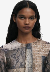 Blusa a fantasia con texture variegate in tonalità neutre, che ricordano le squame e la pelle di rettile, con scollatura rotonda e cuciture sottili.