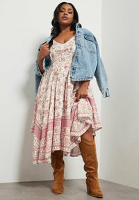 Vestido de largo hasta la rodilla con patrón floral en blanco y rosa, combinado con una chaqueta de denim clara. Botas de ante color canela hasta la rodilla. Tela texturizada.