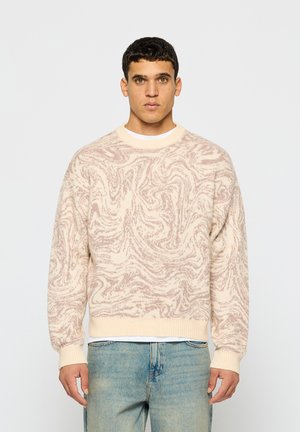 Hellbeiger Pullover mit einem wirbelnden rosa Muster, gerippten Bündchen und Saum sowie einem Rundhalsausschnitt, kombiniert mit hellblauen Jeans.