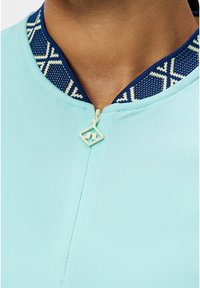 Lichtblauw kledingstuk met een marineblauwe kraag met patroon. Voorzien van een rits met een geometrische trekker. Gladde textuur, strakke lijnen en een aangesloten ontwerp.