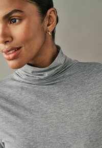 Warmes graues Rollkragenpullover aus weichem Stoff, mit lockerer Passform und subtilen strukturierten Muster. Sichtbarer silberner Creolenohrring.