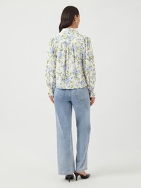 Blommig blus i vitt med blå och gula blommor, puffärmar och hög krage, i kombination med ljusblå denimjeans och svarta klackar.