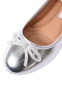 Scarpa da balletto piatta con tomaia argentata metallizzata e punta rotonda, decorata con un delicato fiocco di satin nella parte anteriore.