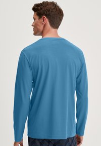 Long-sleeve shirt in bright blue fabric. Smooth texture, round neckline, and a relaxed fit. Worn with patterned dark shorts.