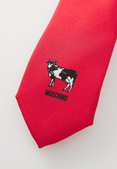 Sarkans zīda kaklasiksnas ar melnbaltu govs grafiku, zaļu loku un zem attēla redzams uzraksts "MOSCHINO".