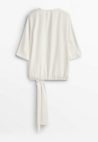 Blusa bianca con una vestibilità ampia, maniche a tre quarti larghe, vita elasticizzata e un dettaglio annodato sul retro. Tessuto liscio e leggero.