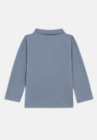 Μπλε πόλο μπλουζάκι με μακριά μανίκια για νήπια ξαπλωμένο επίπεδα, δείχνοντας την πίσω πλευρά με ριπ με κολάρο και απλό ράψιμο.