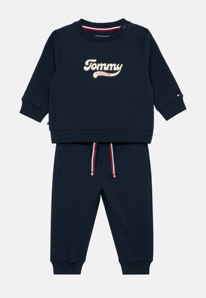 Navy blue two-piece tracksuit with a crewneck sweatshirt and jogger pants. Features "Tommy" logo and red, white, blue drawstring accents.
