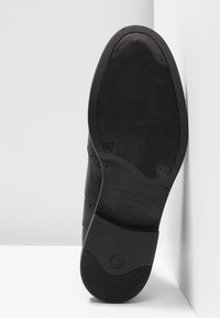 Semelle de chaussure habillée en cuir noir avec une semelle texturée antidérapante, le nom de la marque "Vagabond Shoemakers" et la taille 37 visibles sur une surface blanche.