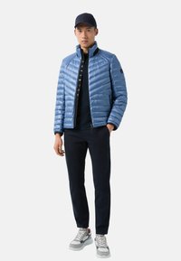 Light blue puffer jacket with horizontal quilting, high collar, and black accents, paired with navy trousers and grey sneakers.