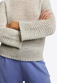 Lichtbeige gebreide trui met een losse, gestructureerde uitstraling en brede geribbelde manchetten, gecombineerd met zachte, lichtblauwe broek.