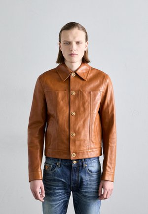 Jachetă din piele maro cu guler, având nasturi aurii și două buzunare frontale. Purtați-o peste blugi blue denim cu o textură decolorată.