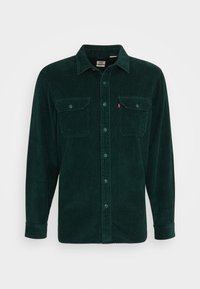 Camicia in corduroy verde con chiusura a bottoni sul davanti, due tasche sul petto e colletto a punta. Presenta righe verticali e una vestibilità relaxed.
