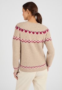Suéter de punto beige con patrones geométricos coloridos en rosa y púrpura en la parte superior y el dobladillo, con un corte relajado y puños acanalados.