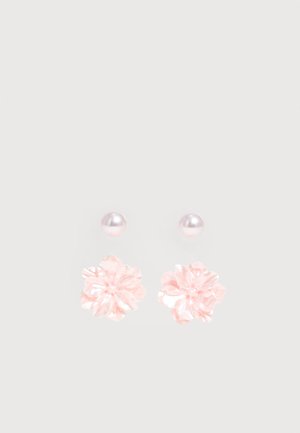 Twee paar oorknopjes, één met kleine ronde parels en één met lichtroze bloemvormige designs, tegen een effen achtergrond.