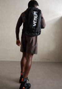 Sac à dos noir avec "VENUM" en lettres blanches en gras, présentant plusieurs compartiments, des bretelles ajustables et une texture de tissu durable.