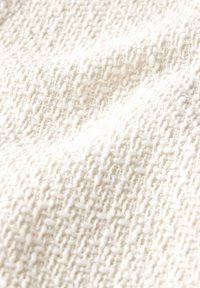 Texturerad krämfärgad tyg med ett vävt mönster, som har en subtil upphöjd design och en mjuk, plyschig yta. Idealisk för klädsel eller plagg.