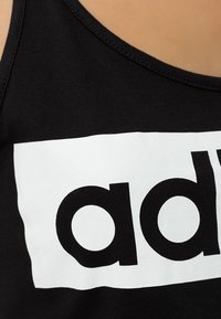 Czarny top na ramiączkach z odważnym, białym, prostokątnym nadrukiem z napisem „add” dużymi czarnymi literami. Gładka bawełniana tkanina z okrągłym dekoltem.